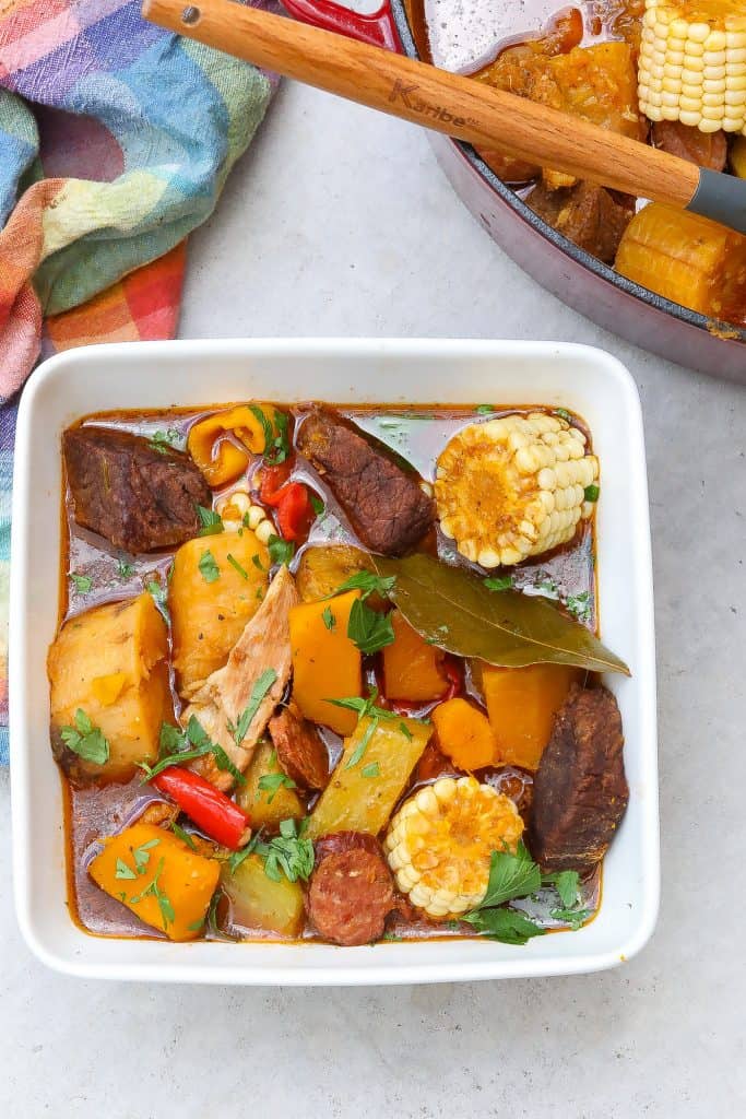 sancho stew in a square white bowl with corn, beef, and potatoes