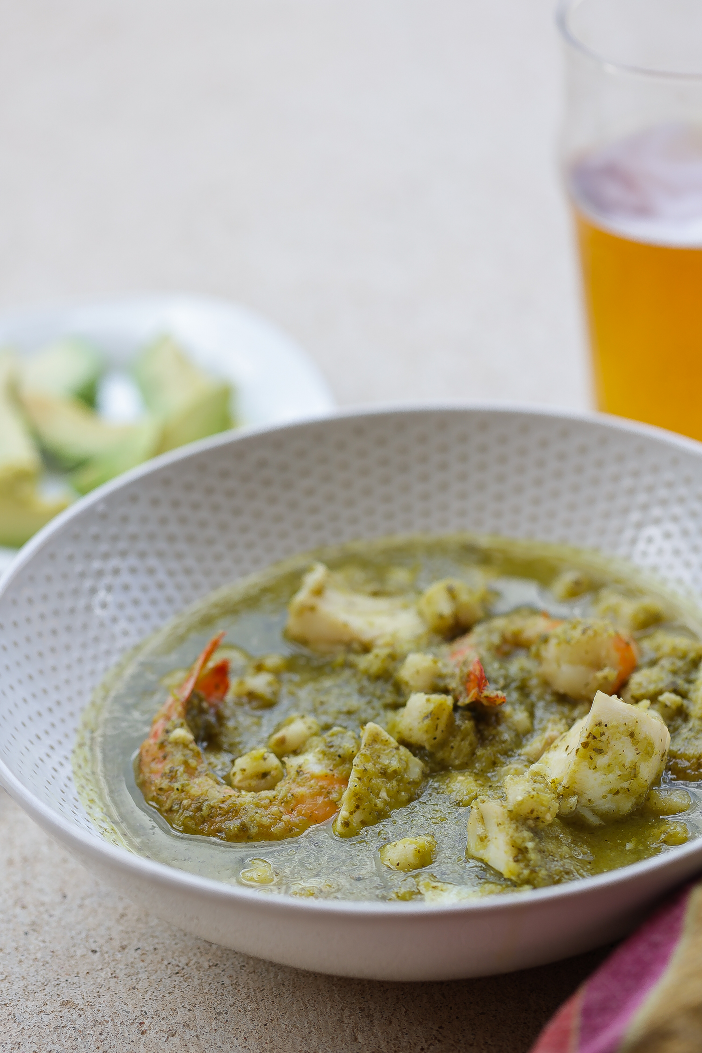 seafood posole verde in a white bowl with avocado