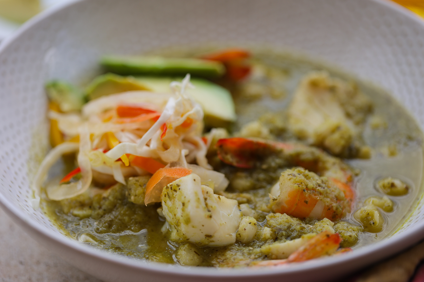 seafood posole in white bowl topped with haitian pikliz