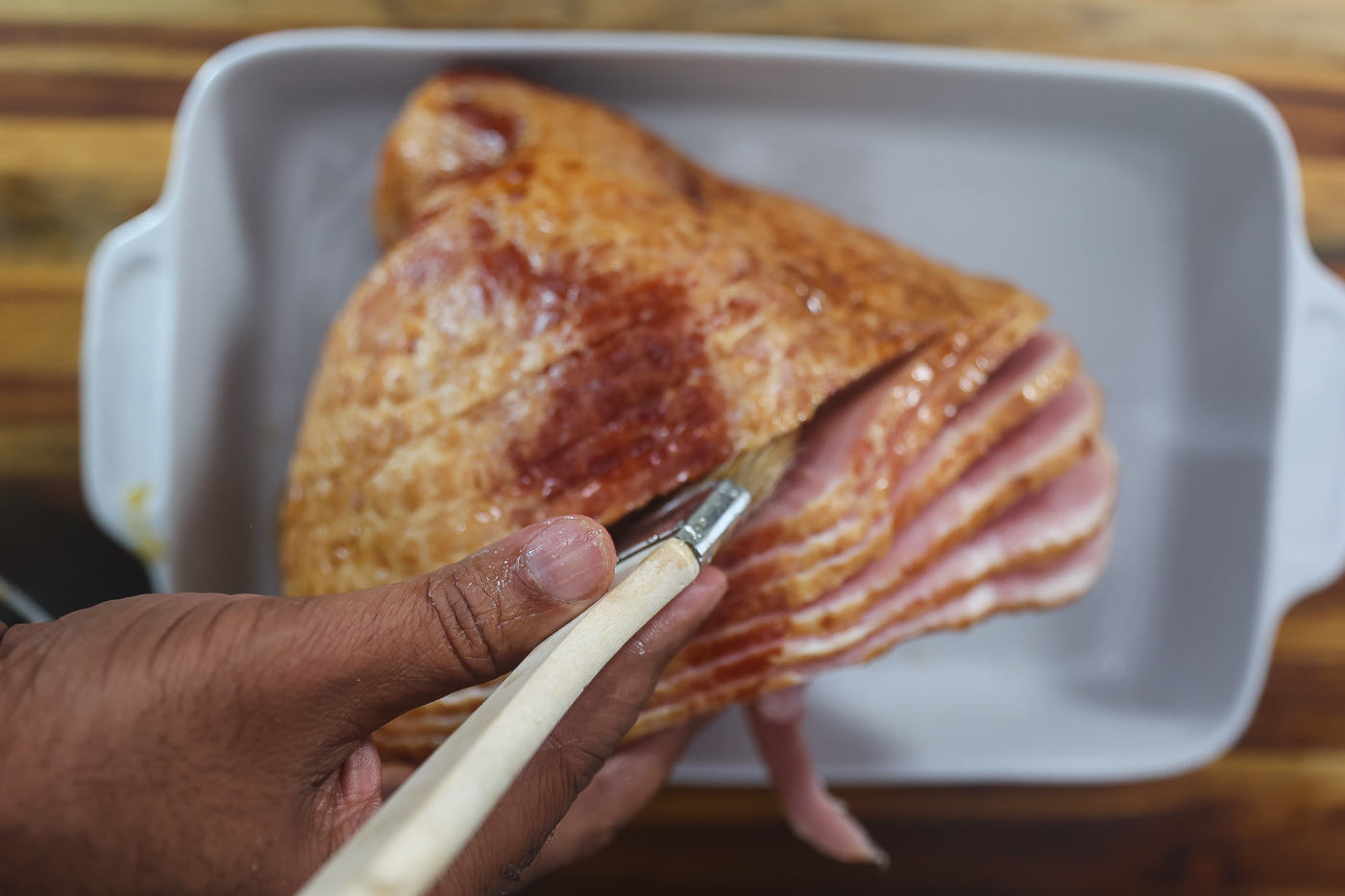 A hand brushing a maple glaze onto a sliced ham