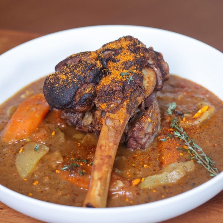 lamb shank on cider based sauce in white plate