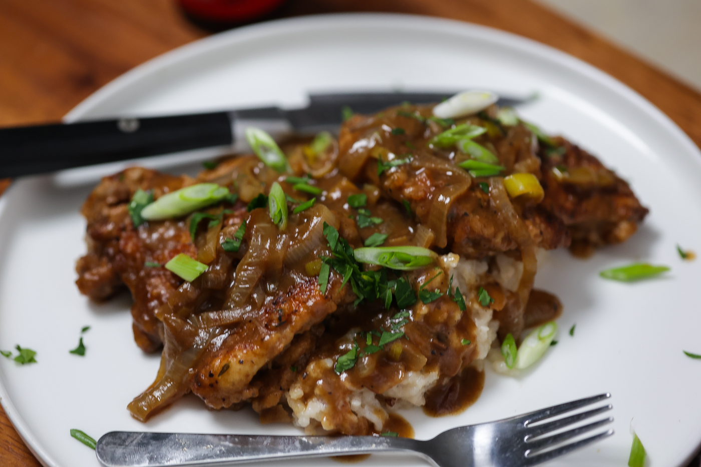 2 smothered chicken thighs sitting on a white plate