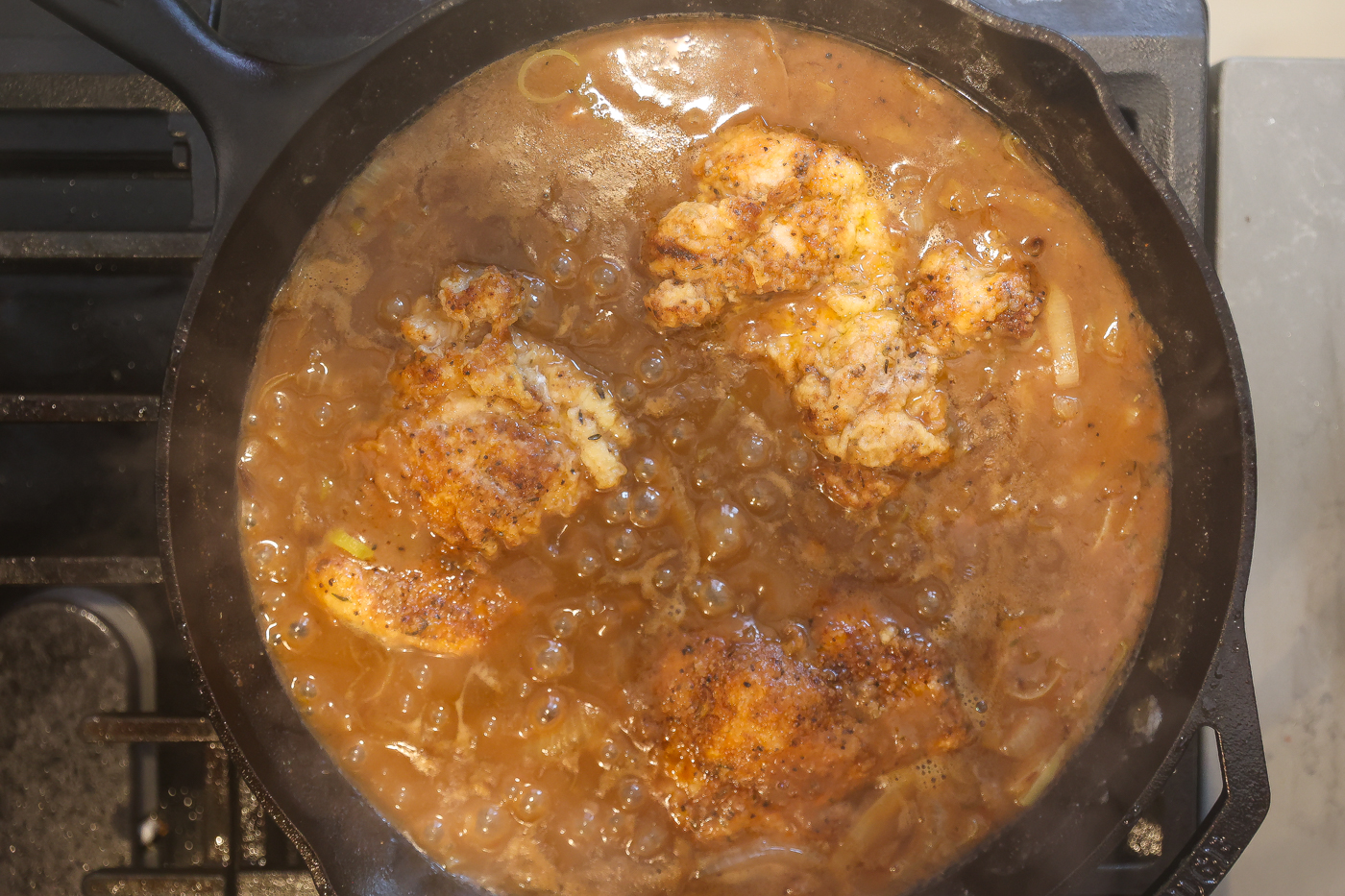 chicken thighs cooking in skillet with gravy