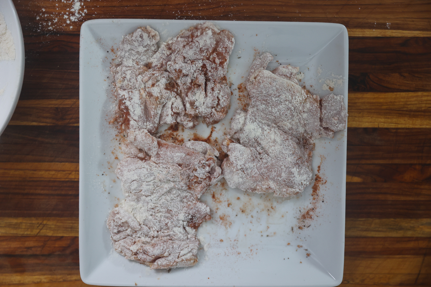 floured chicken thighs sitting on a white plate