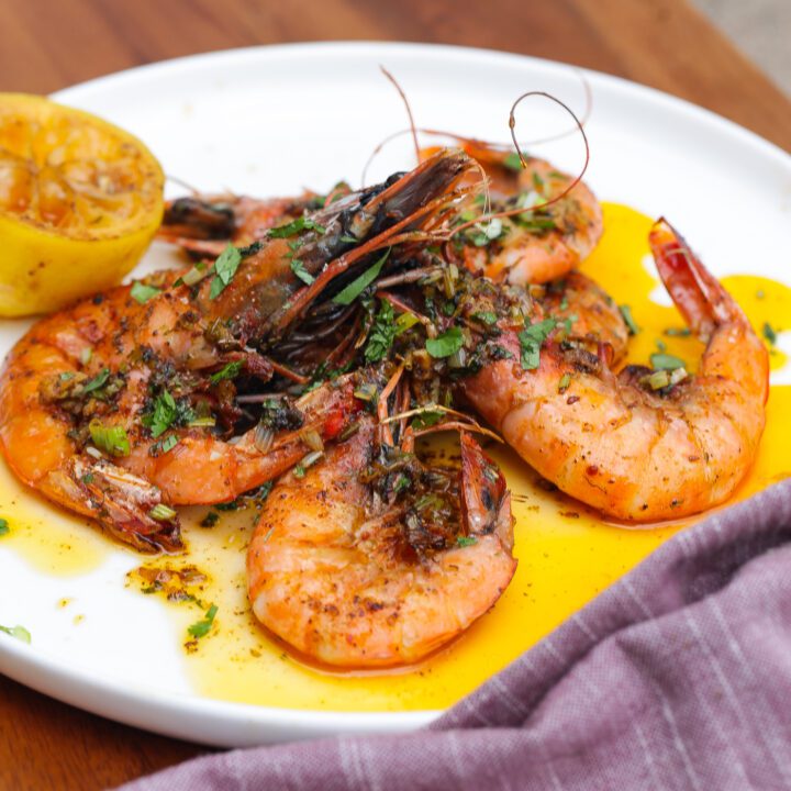 lemon garlic butter shrimp stacked on white plate topped with fresh cilantro