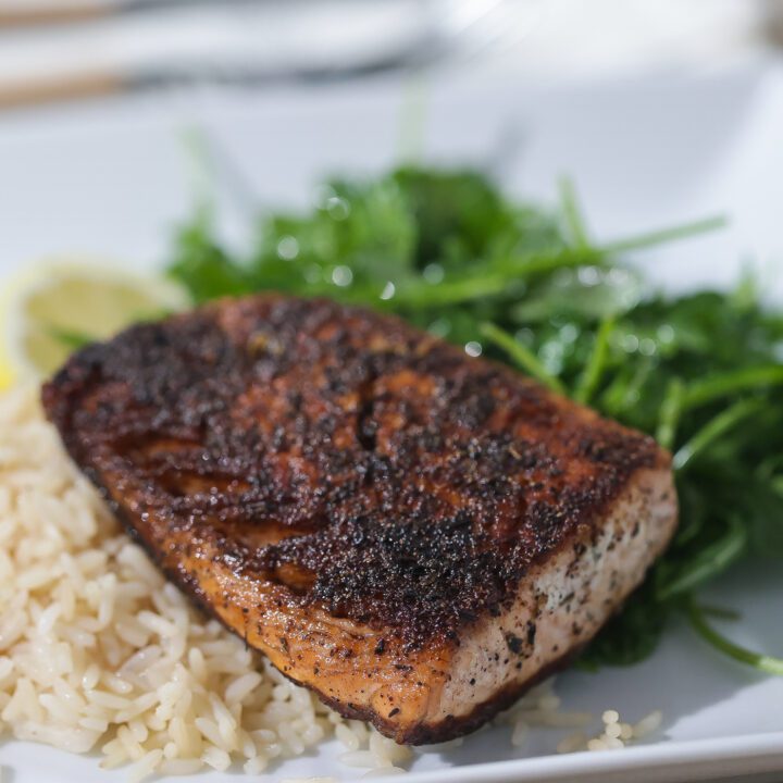 blackened salmon on white plate with rice and greens